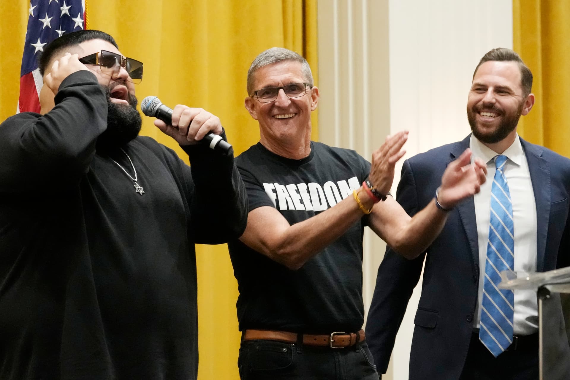 AP/Marta Lavandier Gen. Michael Flynn (retired), center and Pastor Jackson Lahmeyer listen to Jimmy Levi sing during the ReAwaken America Tour, Pastors for Trump event, October 12, 2023, in Doral, Florida.