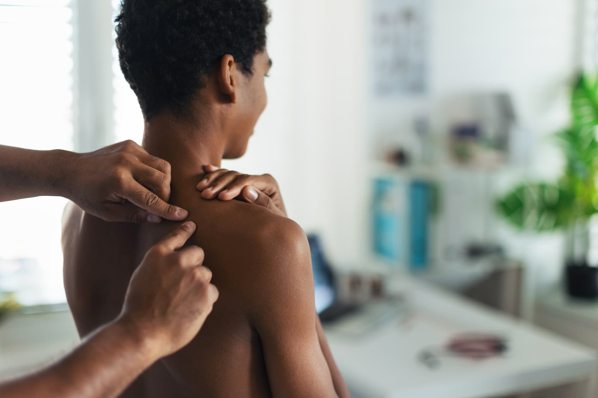 A medical doctor examines acne on a teenager's back. 