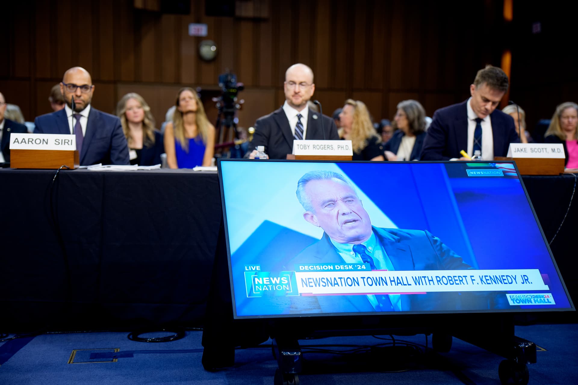 Health and Human Services Secretary Robert F. Kennedy Jr. is depicted on a monitor during a short video as Attorney Aaron Siri, Brownstone Institute fellow Toby Rogers, and Dr. Jake Scott, an infection disease specialist at Stanford University's School of Medicine, appears at a Senate Homeland Security and Government Affairs Subcommittee Hearing on Capitol Hill on September 9, 2025.