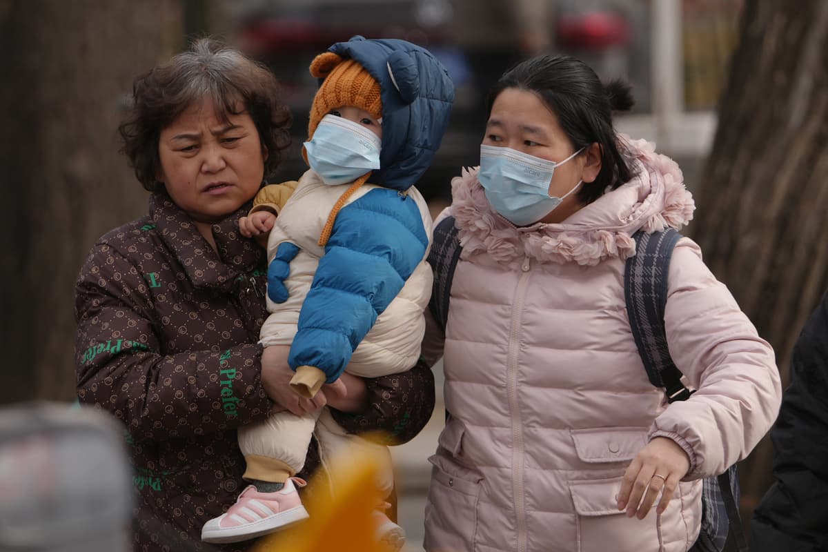 Women carry a toddler across a street at Beijing, January 19, 2026. 