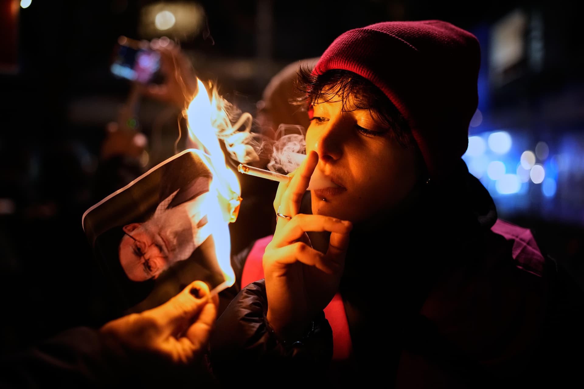 A protester smokes a cigarette after lighting it off a burning poster of Iran's Supreme Leader Ayatollah Ali Khamenei during a demonstration at Berlin, in support of the nationwide mass protests in Iran against the government, January 14, 2026. 