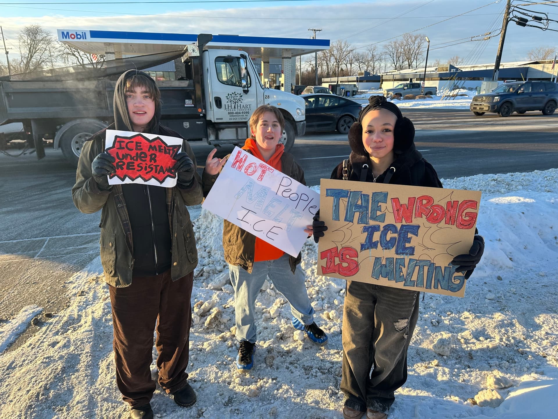 From left, Asher O'Donnel, Ryan Maddox  and Amari Perez-Wayner hold signs as several dozen Groves High School students walk out of morning class on January 30, 2026 in Birmingham, Michigan. 