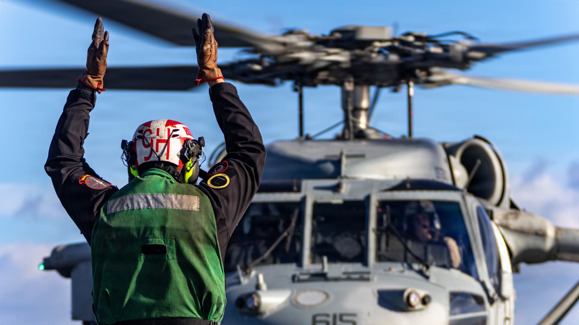 A U.S. Navy Sailor signals an MH-60S Sea Hawk helicopter, attached to Helicopter Sea Combat Squadron 9, from the flight deck of Gerald R. Ford.