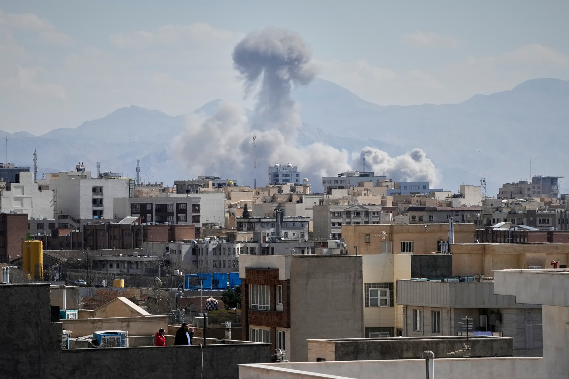 People watch from a rooftop as a plume of smoke rises after a strike on Tehran, Iran, Sunday, March 1, 2026.
