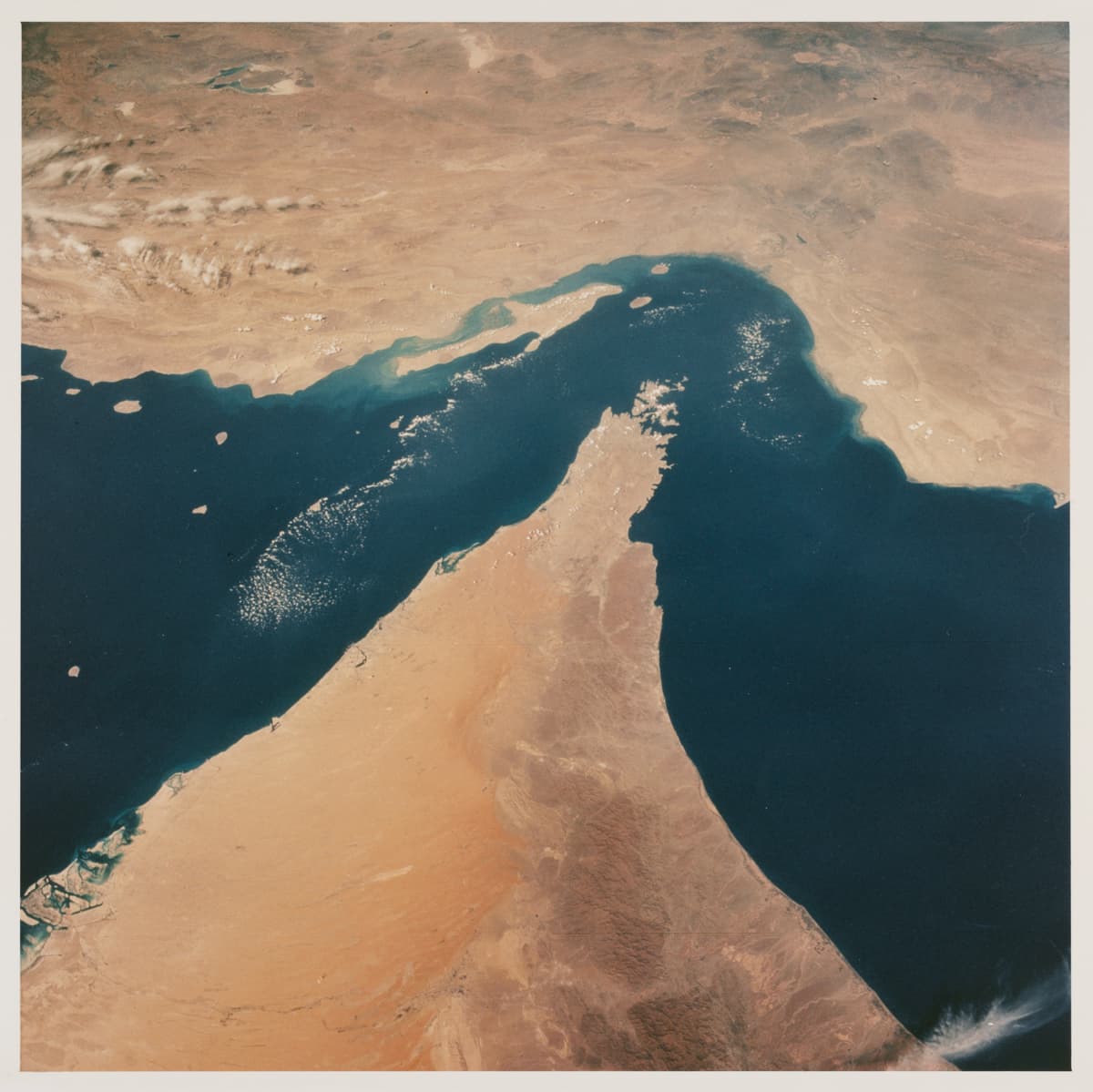 View looking north showing the Strait of Hormuz, connecting the Gulf of Oman with the Persian Gulf, with the Zagros Mountains and Qeshm Island of Iran in the background, and areas of Oman, Muscat and the United Arab Emirates in the foreground, as seen from the Space Shuttle Columbia during shuttle mission STS-52 in 1992. 