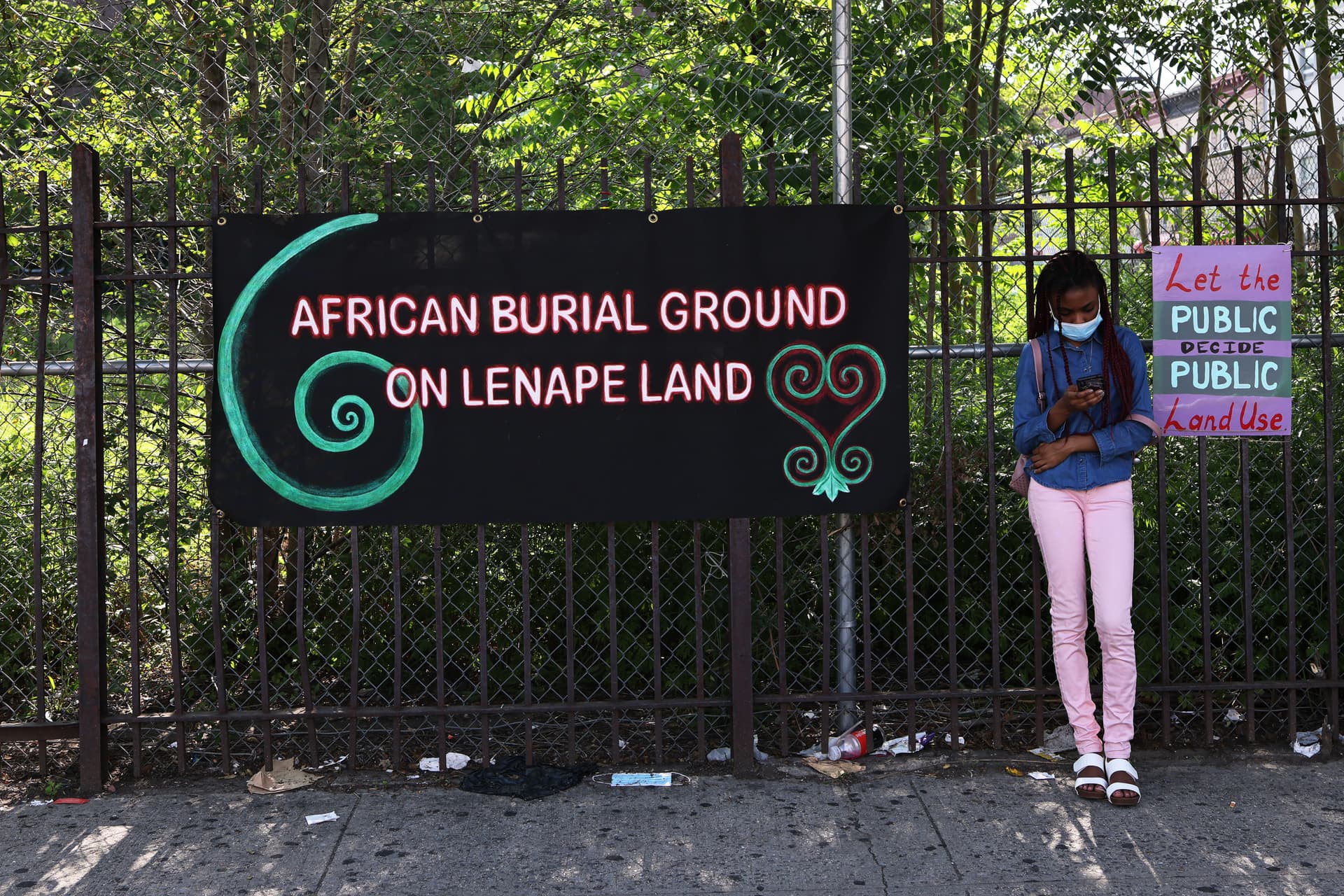 A young girl leans next to banners on a fence blocking a lot believed to be a burial ground for enslaved Africans at the Flatbush neighborhood of Brooklyn, New York, on June 9, 2021.