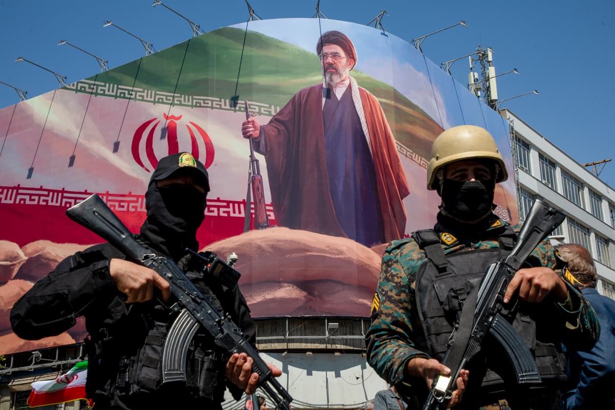 Members of the Iranian security forces stand guard under a large portrait of Iran's new supreme leader, Mojtaba Khamenei, at Tehran on April 9, 2026.