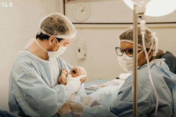 A surgeon and a medical assistant examine a crying, newly born infant. Growing numbers of American parents are refusing an injection of vitamin K routinely provided at birth.