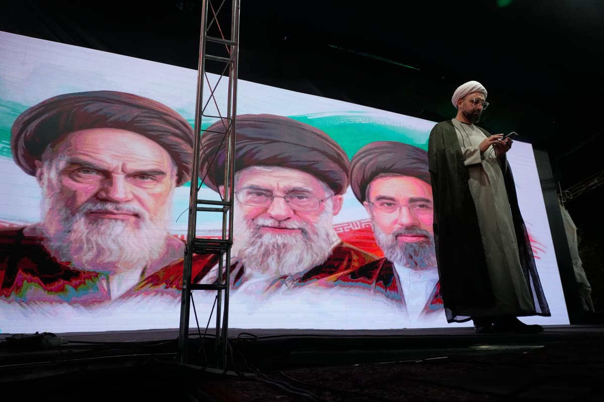 A cleric checks his cell phone on stage in front of a screen displaying portraits of the late Iranian revolutionary founder Ayatollah Khomeini, left, late Supreme Leader Ayatollah Ali Khamenei, center, and Supreme Leader Ayatollah Mojtaba Khamenei, during a pro-government gathering in Tehran June 7, 2026. 