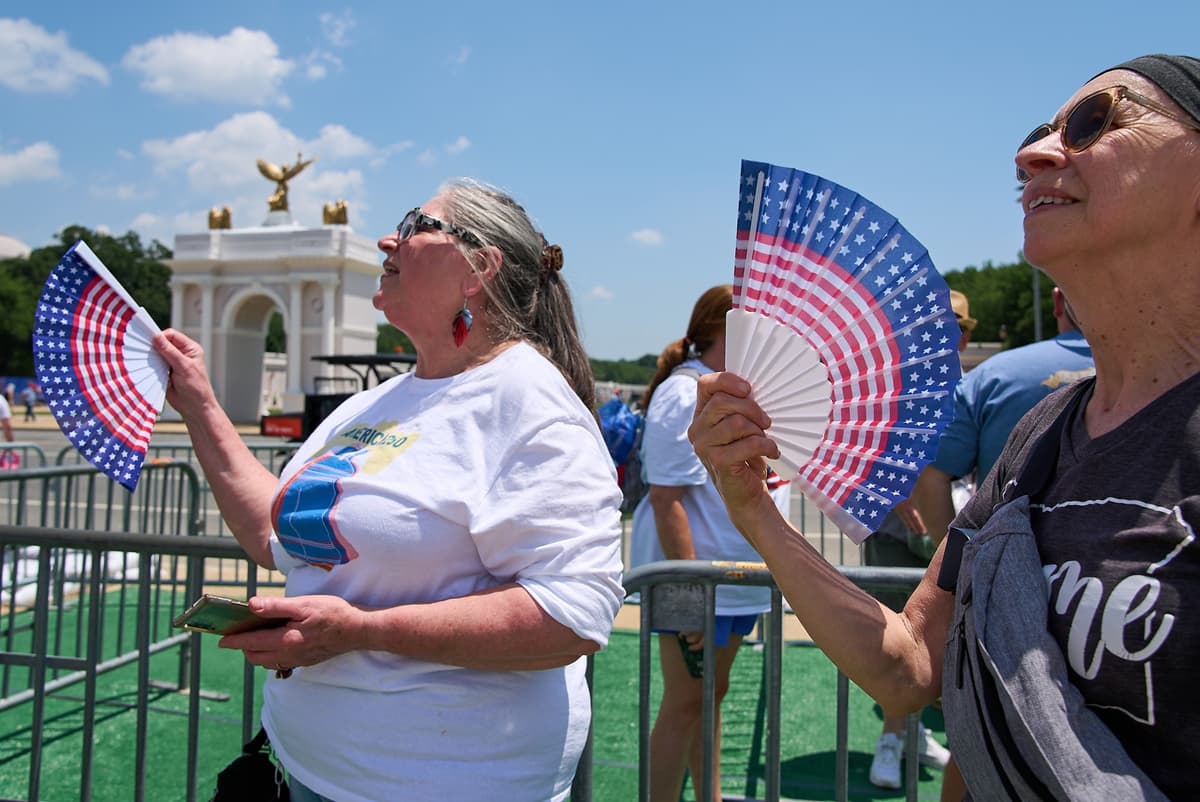 Visitors fan themselves while waiting in line for the ferris wheel at the Great American State Fair at Washington, D.C, on July 1, 2026.