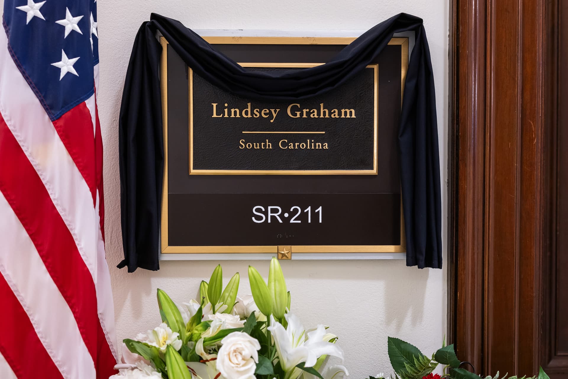 Flowers surround the covered plaque outside the office of the late Senator Lindsey Graham at Russell Senate Office Building on July 14, 2026.