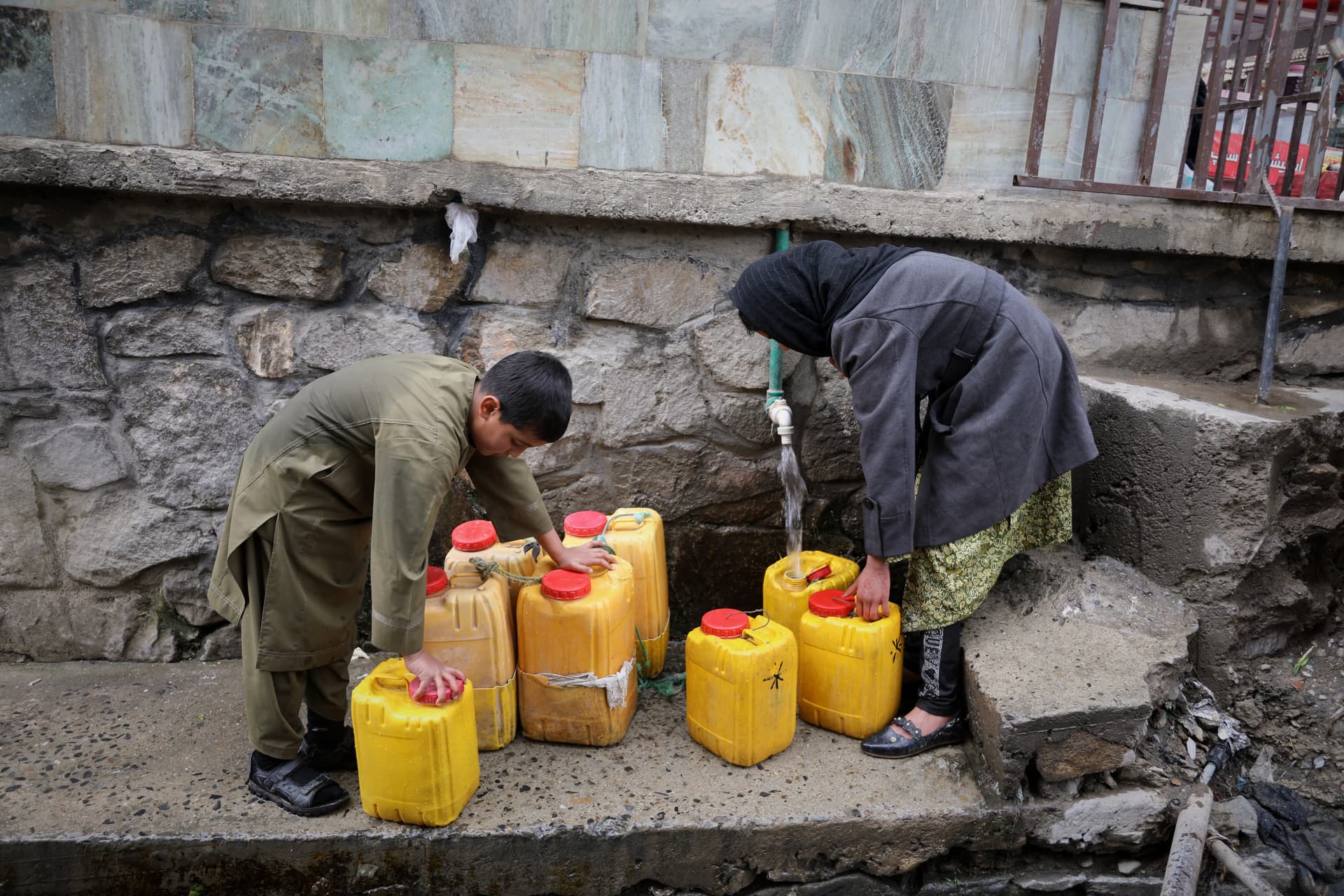 A boy and a girl collect water from a hose connected to a well at a mosque at Kabul, Afghanistan, on April 2, 2026.