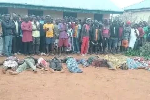 Community members stand behind the bodies of victims of a massacre at the village of Naridon in Nigeria ahead of a mass burial on August 1, 2026.