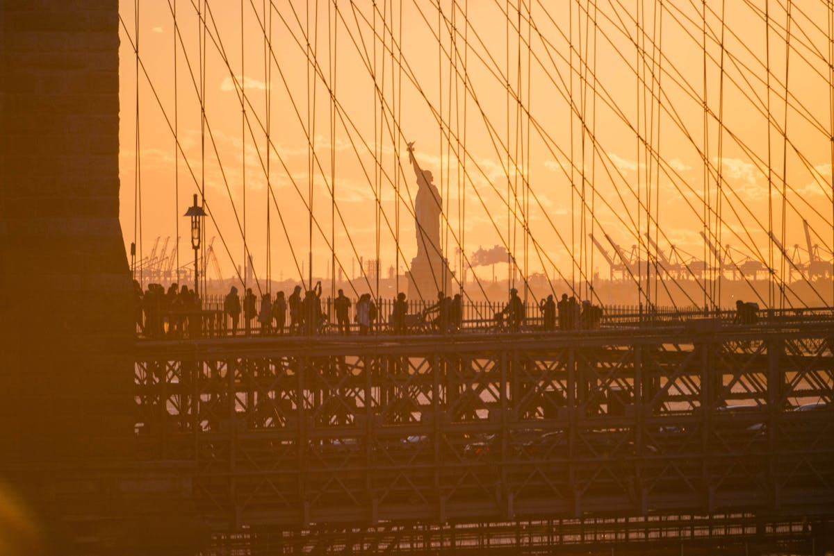 The sun rising behind the Brooklyn Bridge with a view of the Statue of Liberty.