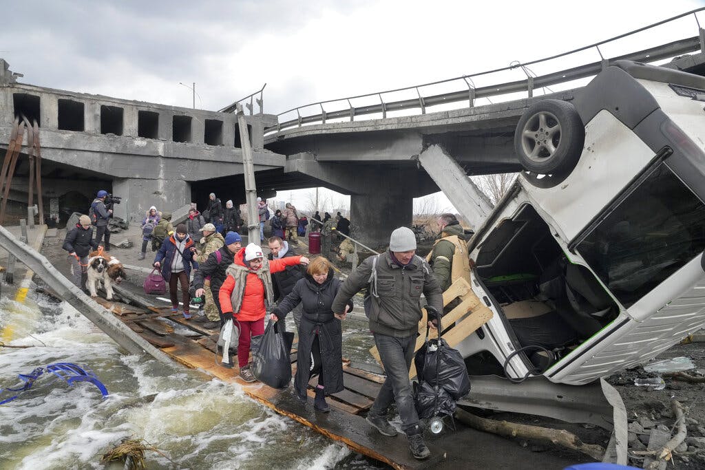 People cross an improvised path under a destroyed bridge while fleeing the town of Irpin close to Kiev, March 7, 2022. AP/Efrem Lukatsky
