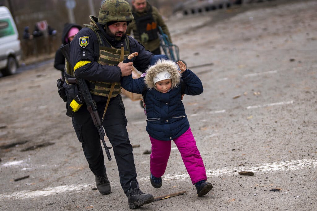 A Ukrainian police officer runs while holding a child as sounds of artillery echo nearby at the outskirts of Kiev, March 7, 2022. AP/Emilio Morenatti