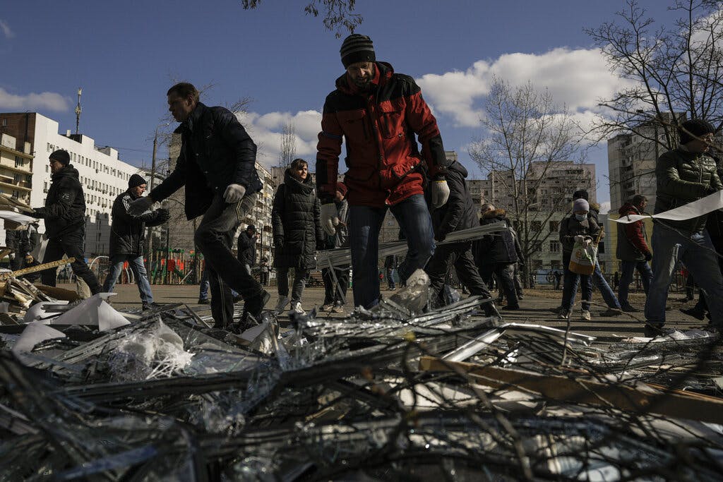 People clear debris outside a medical center damaged after parts of a Russian missile, shot down by Ukrainian air defense, landed on a nearby apartment block, according to authorities, in Kyiv, Ukraine, Thursday, March 17, 2022. AP Photo/Vadim Ghirda
