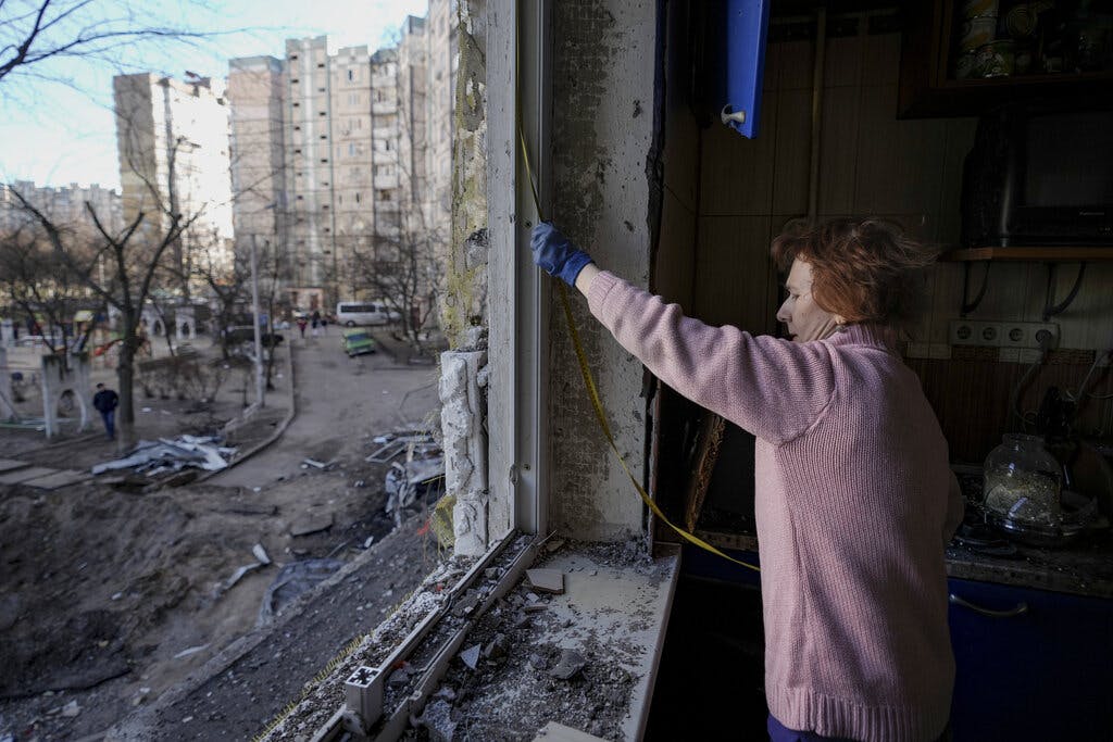 A woman measures a window before covering it with plastic sheets in a Kiev building damaged by a bombing, March 21, 2022. AP/Vadim Ghirda