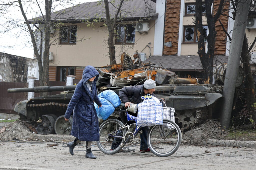 Civilians walk past a tank destroyed during heavy fighting in an area controlled by Russian-backed separatist forces at Mariupol April 19, 2022. AP/Alexei Alexandrov