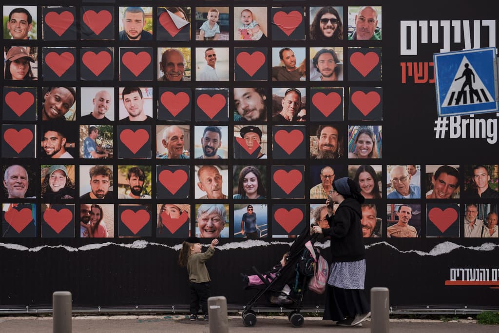 AP/Leo Correa A woman and her children walk past a wall with photographs of hostages who were kidnapped by Hamas terrorists on October 7.