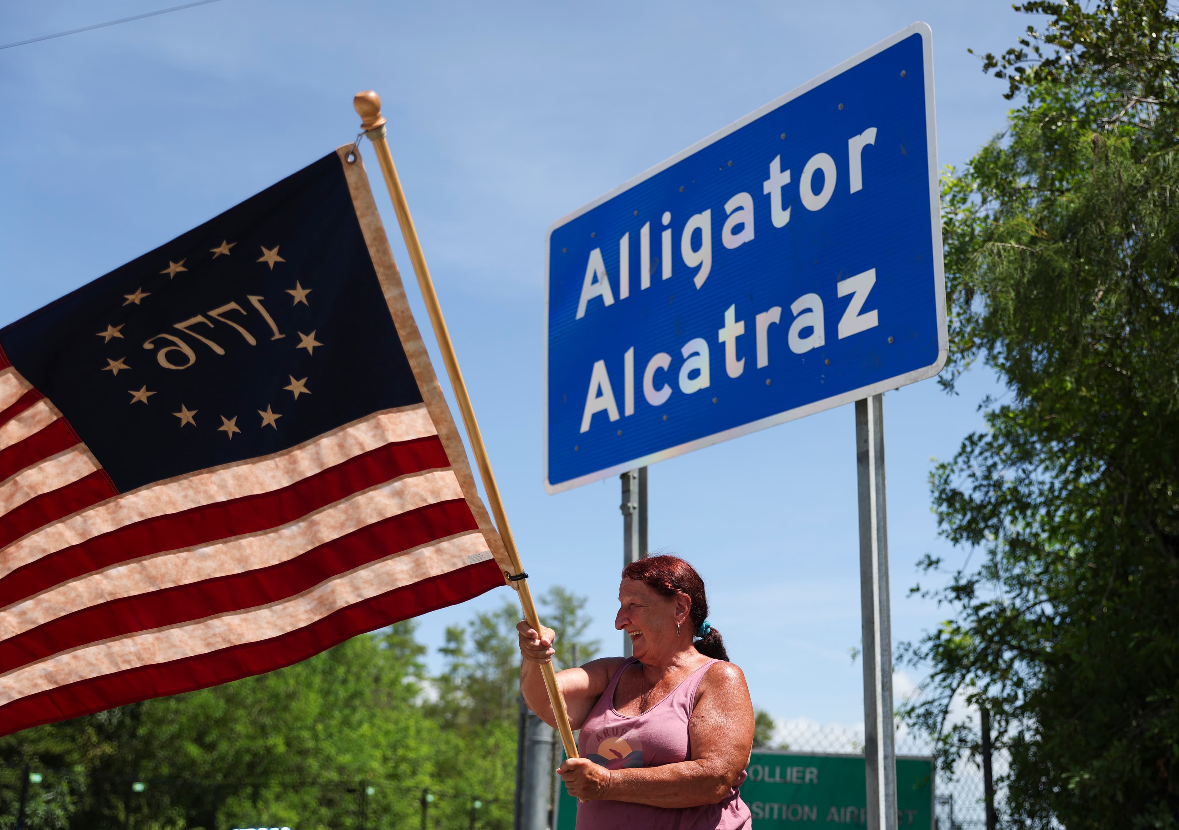 A woman waves a flag outside of the Dade-Collier Training and Transition facility, also known as “Alligator Alcatraz,” at Ochopee, Florida, on July 12, 2025. A woman waves a flag outside of the Dade-Collier Training and Transition facility, also known as “Alligator Alcatraz,” at Ochopee, Florida, on July 12, 2025.