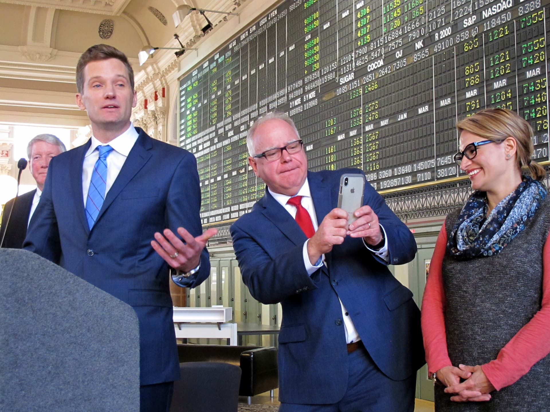 AP Photo/Doug Glass Tim Walz, center, then Minnesota's governor-elect, leans to get a picture of the wife and children of Steve Grove, left, who'd been named Walz's new commissioner of economic development, Friday, Jan. 4, 2019, at the Minneapolis Grain Exchange. Grove is now CEO of the Minneapolis Star Tribune.