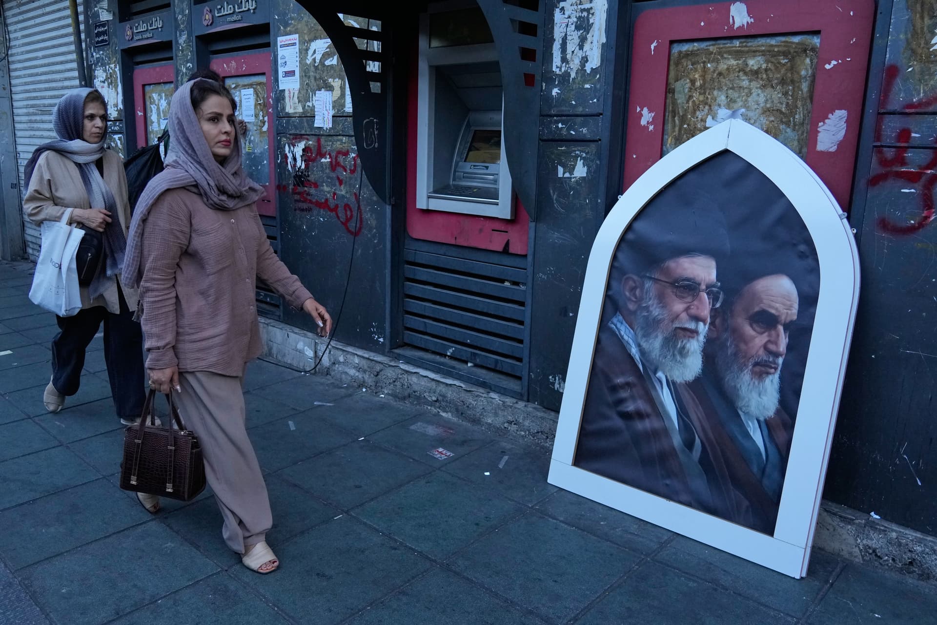 AP/Vahid Salemi) Pedestrians walk past a poster showing the slain Iranian Supreme Leader Ayatollah Ali Khamenei, left, and the late revolutionary founder Ayatollah Khomeini on a sidewalk at the Islamic Revolution square in Tehran, Iran, June 14, 2026.