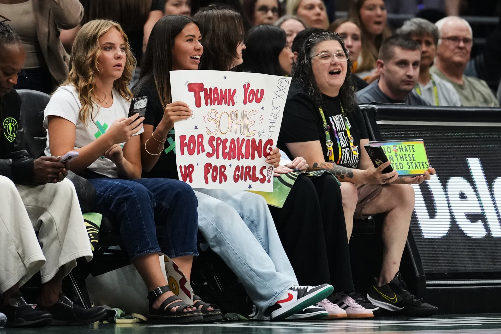 AP/Lindsey Wasson A fan holds a sign for Indiana Fever guard Sophie Cunningham for her comments on transgender athletes during the first half of a WNBA basketball game, July 28, 2026, at Seattle.