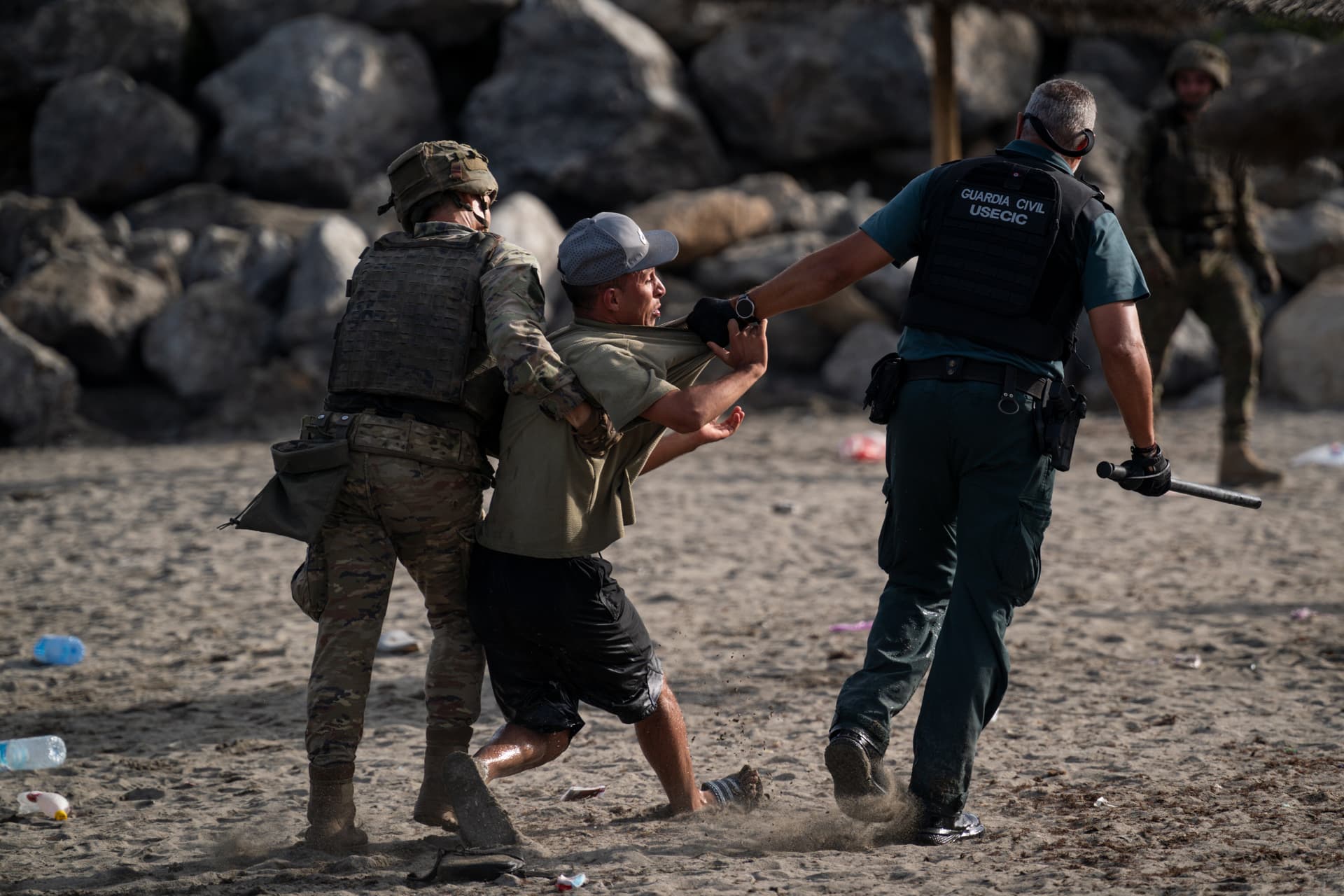 Adri Salido/Getty Images Security forces detain one of the thousands of would-be migrants who have flooded into the Spanish enclave of Ceuta on July 31, 2026.