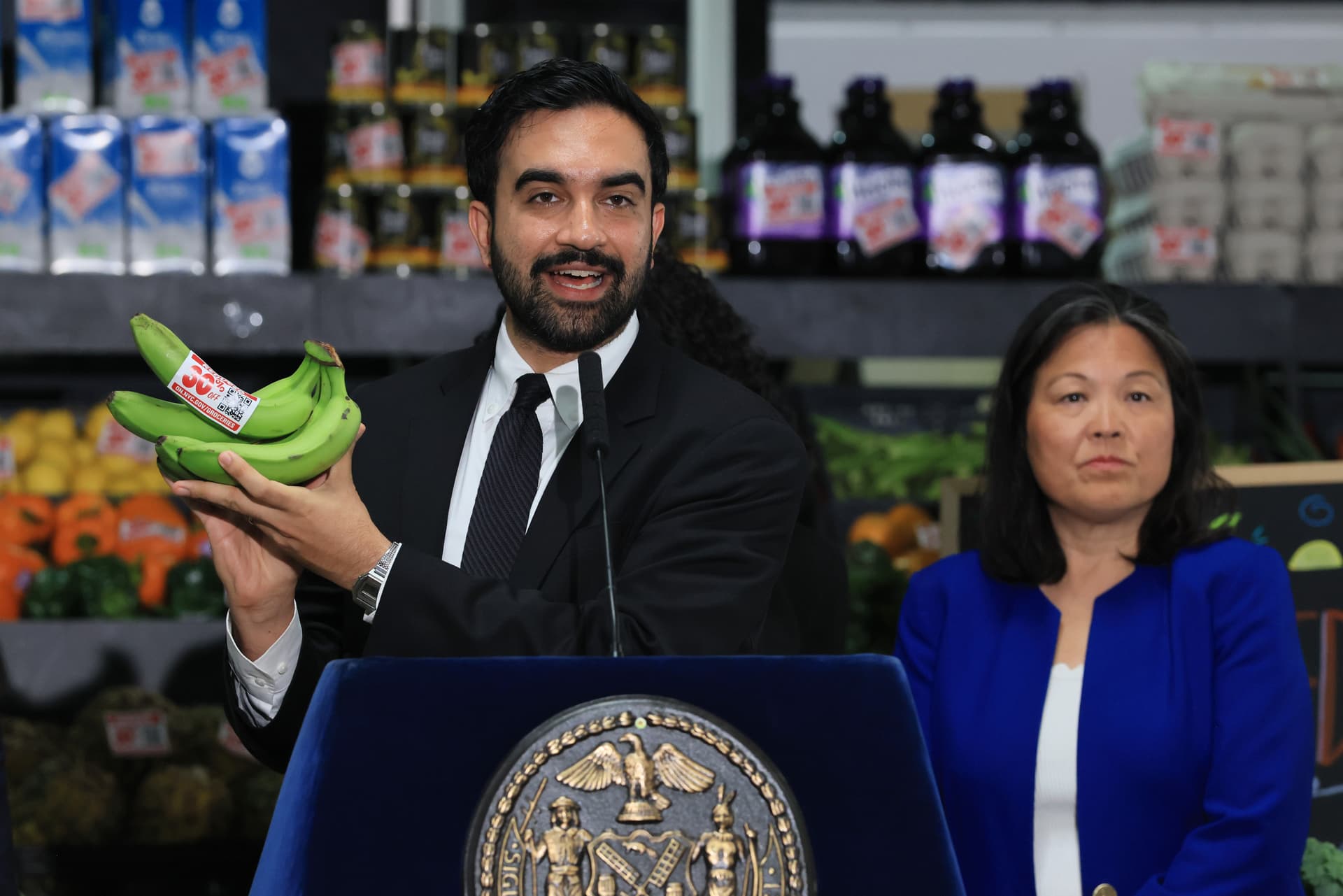 NEW YORK, NEW YORK - JULY 27: New York City Mayor Zohran Mamdani holds up bananas as he speaks at a food distribution center on July 27, 2026 in the Brooklyn borough of New York City. Mamdani announced that the five upcoming city-owned grocery stores will offer a 30 percent discount on produce, meat, bread, and milk when they begin to open next year. The discount on essential items will potentially save shoppers an estimated $90 a month, or roughly $1,000 a year, as prices for food and other items continue to rise throughout the country. The mayor has pledged one community grocery store for each borough. (Photo by Spencer Platt/Getty Images) Featured image for City To Offer Financial Boost to Stores Threatened by Mamdani’s Gastronoms