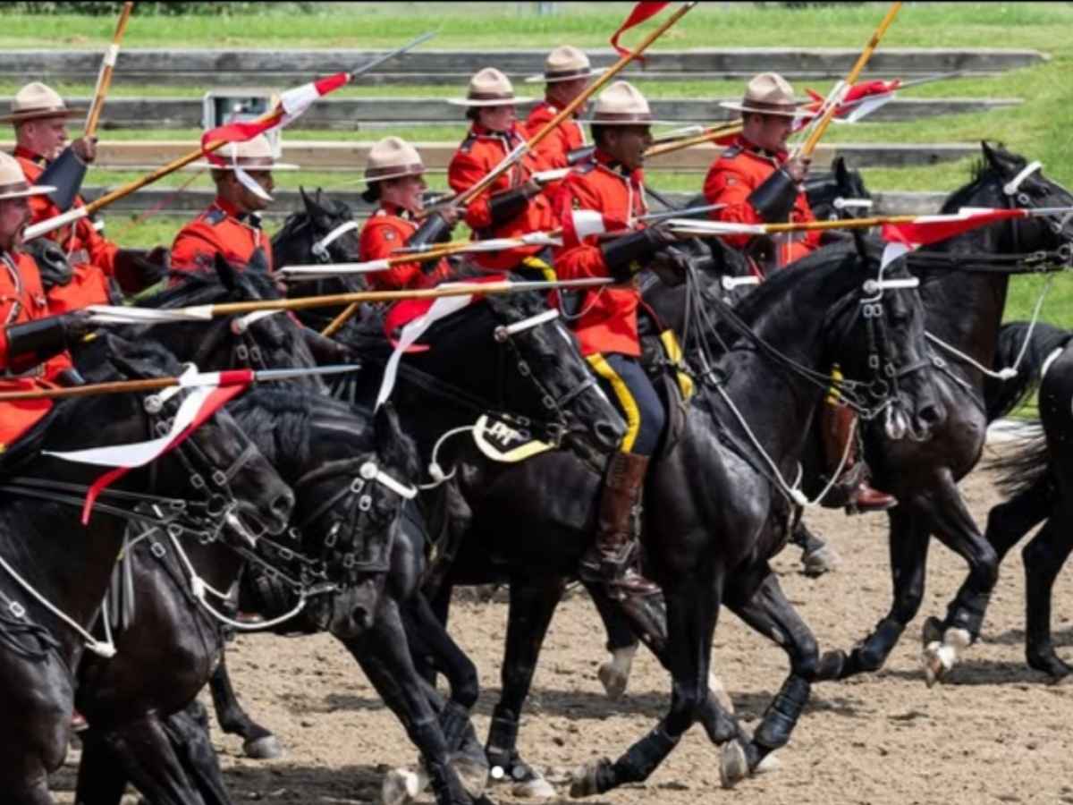 Royal Canadian Mounted Police via Instagram. This photograph captures members of the Royal Canadian Mounted Police riding in formation during a parade, dressed in their iconic red serge uniforms and riding black horses.