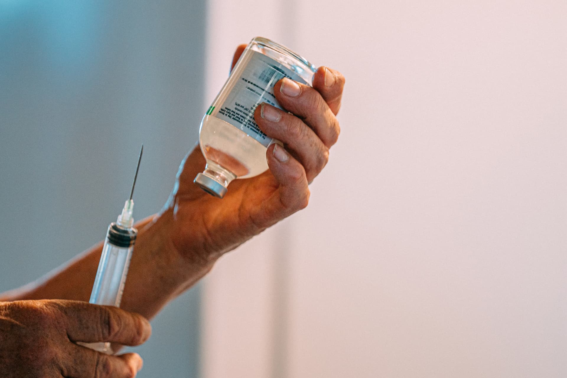 Getty Images. A doctor prepares to draw clear liquid from a glass vial with a large hypodermic syringe.