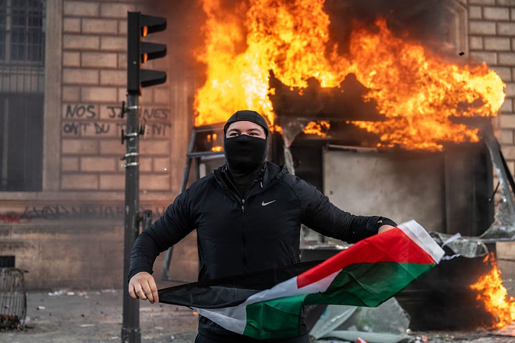 Guy Smallman/Getty Images A protester holds a Palestinian flag as a bus stop burns at Paris, France.